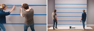 A couple is using blue painter's tape on a wall.