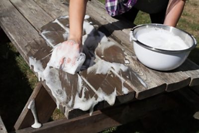 A person prepping a picnic table for paint or stain.