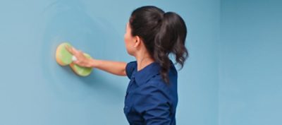 A woman washing a wall with a sponge.