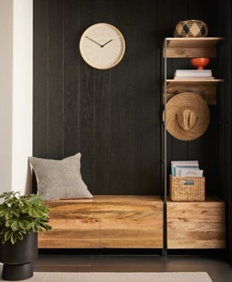 Wooden bench sitting area with black wood paneled walls with a clock next to a plant.
