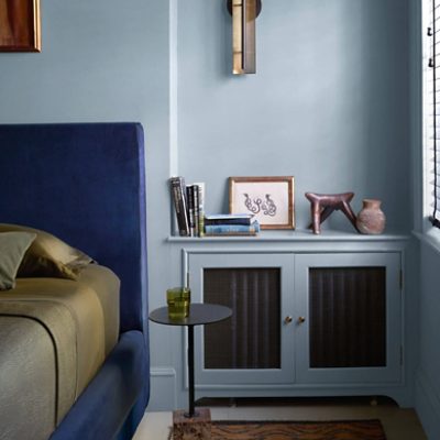 A bedroom with bluish gray walls, a bed with a royal blue headboard and golden sheets next to a small circular table.