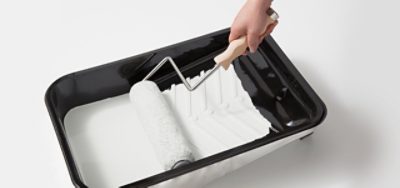 A paint tray with white paint and a paint brush.