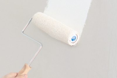 Applying white paint to a wall with a roller.