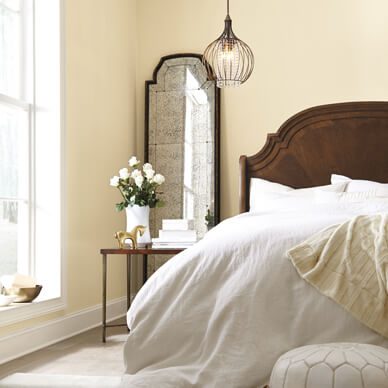 A comfy bed with tall mirror against a white wall.