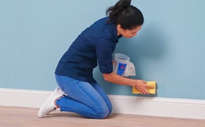 A woman cleaning a light blue wall with a sponge.