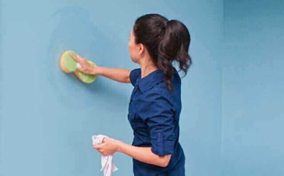 A woman is cleaning a wall with a sponge.