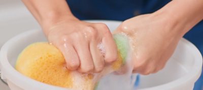 A woman wringing out a sponge with soap and water.