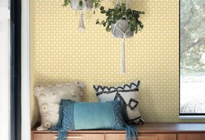 An entryway with bench and pillows and a yellow fan design wallpaper wall.