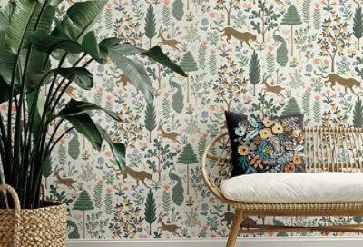 A wicker bench with cushion next to a large leafy potted plant against a wallpapered wall.