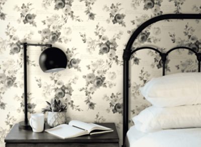 Neutral wall with grey floral print, bedside table with black lamp next to a bed with black bedfraim.