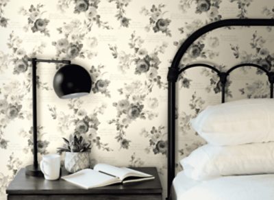 Neutral wall with grey floral print, bedside table with black lamp next to a bed with black bedframe.