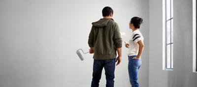 A young couple preparing to paint a wall with rollers.