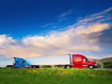A banner showing two trucks, one blue and one red, driving on a road under a partly cloudy sky.